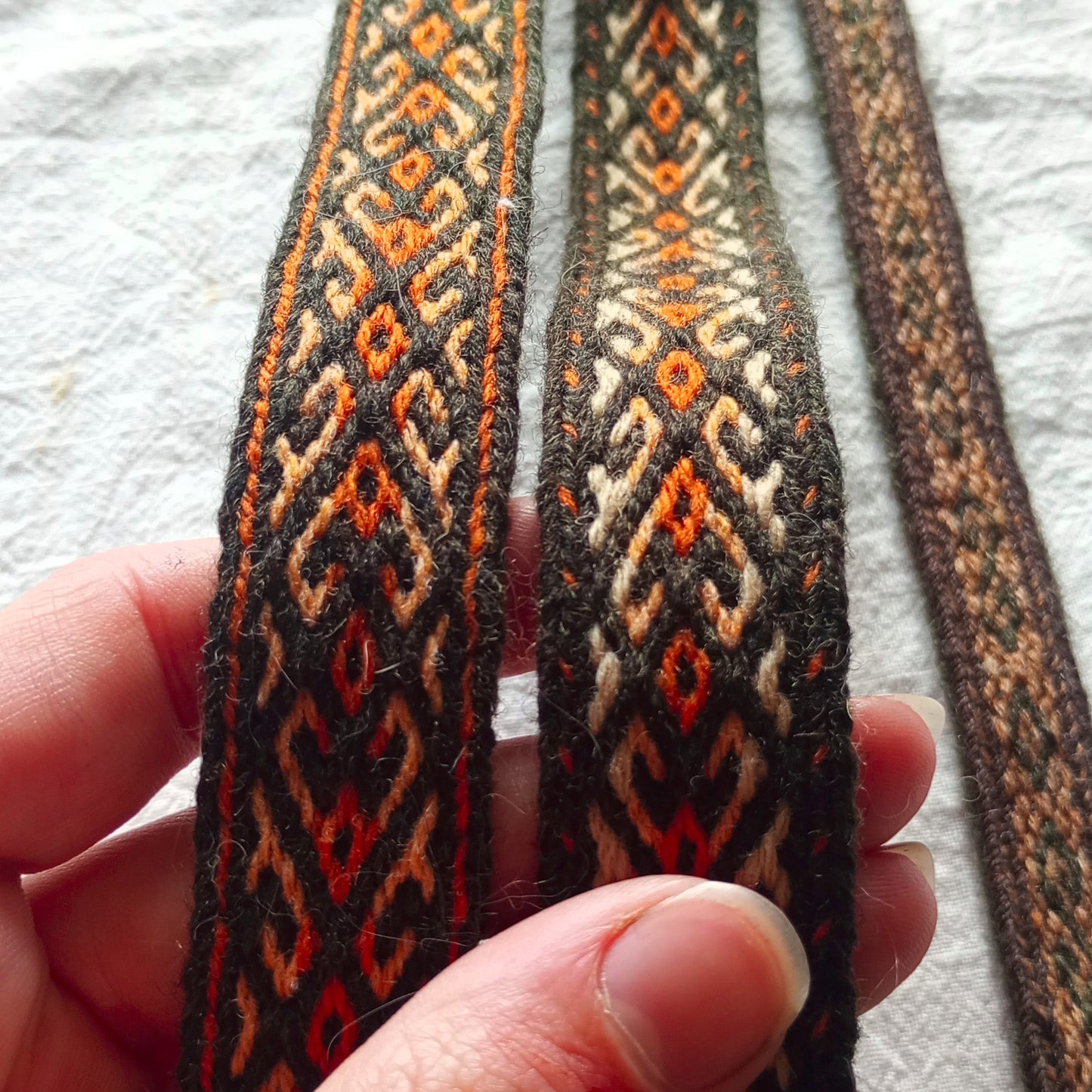 A hand holding a section of fabric with a green and orange geometric pattern, typically used for weaving.