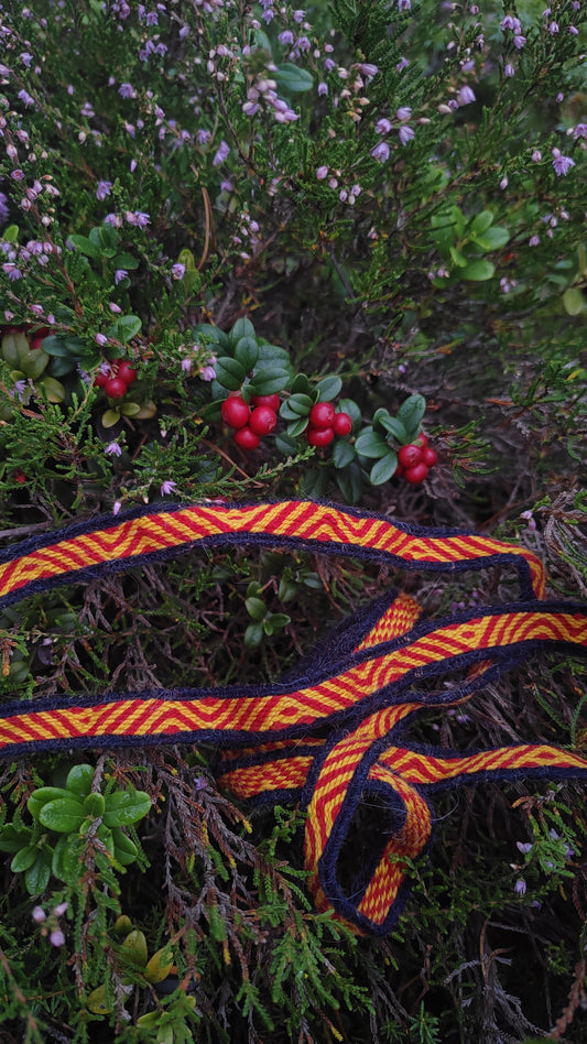 Viking age tablet woven ribbon with red and yellow pattern on a natural background with berries and greenery.
